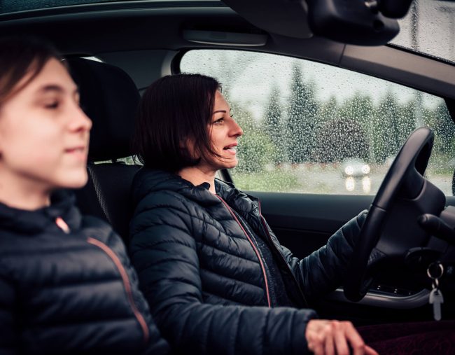 A woman driving with her daughter in the passenger seat. It's raining.